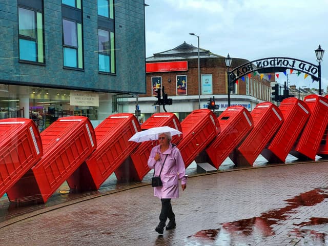 A woman with an umbrella walks past the famous 'Out of Order' telephone boxes sculpture in Kingston upon Thames, UK.