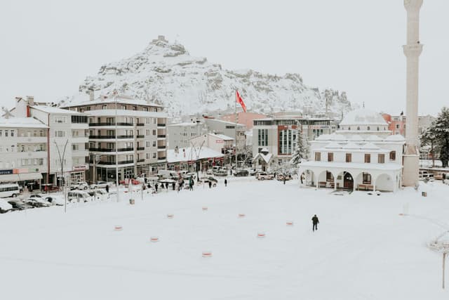 A picturesque winter scene featuring a mosque and snow-covered mountain in a town square.