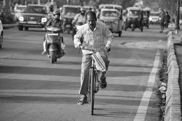 A South Asian man rides a bicycle on a busy street in Bhubaneswar, India, amidst traffic.