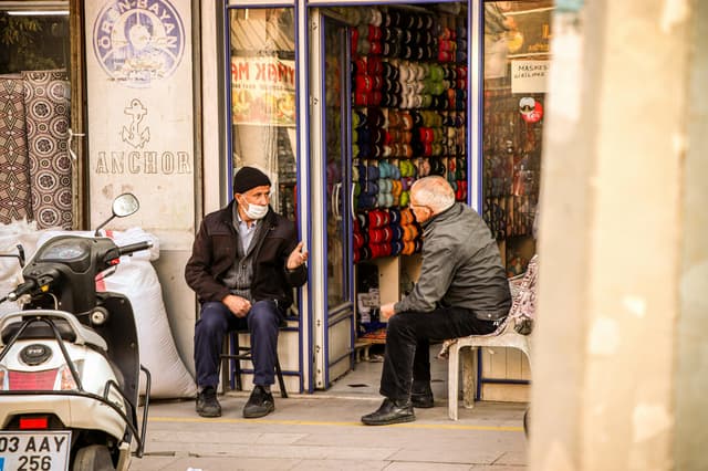 Two elderly men in Afyonkarahisar, Turkey, engage in conversation outside a yarn shop.