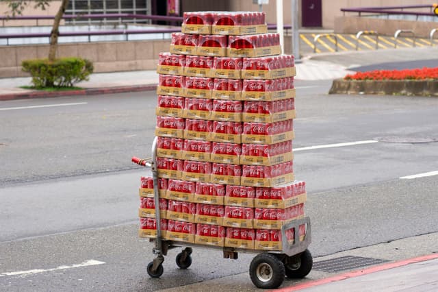 Stacked Coca Cola cans on a delivery cart in a city street, showcasing urban distribution.