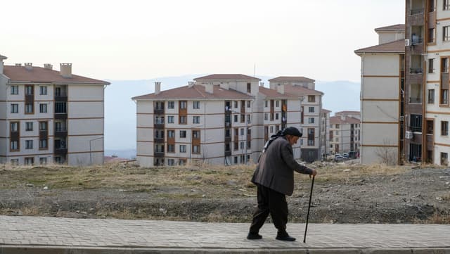 Senior man using a walking stick strolls past residential buildings in Şırnak, Türkiye.
