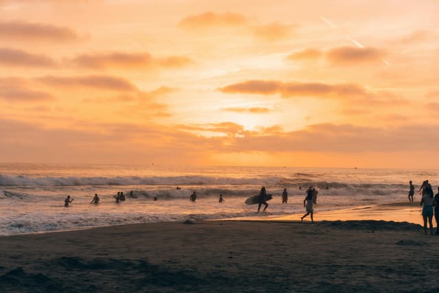 A vibrant sunset over a beach with surfers and swimmers enjoying the ocean waves.