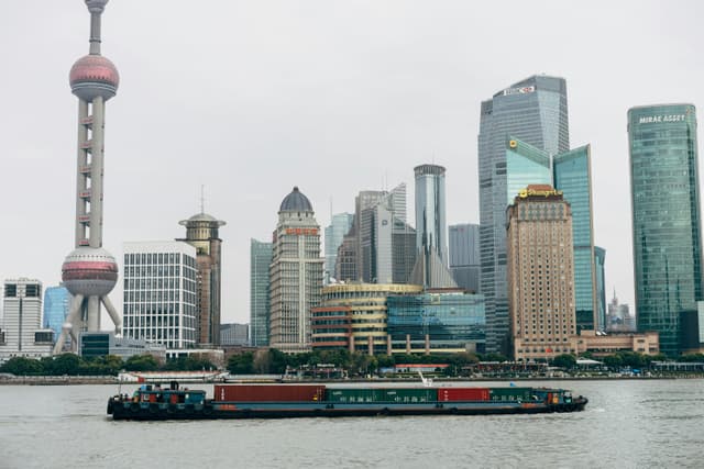 Panoramic view of Shanghai skyscrapers and a cargo boat on Huangpu River, capturing the city's modern architecture.