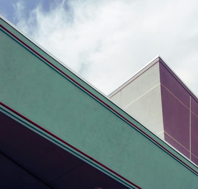 Low-angle shot of modern geometric building with glass reflection under a cloudy sky.