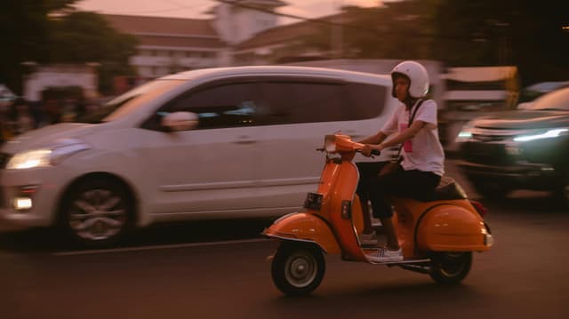 A man rides a vintage Vespa through traffic at dusk in West Java, Indonesia.