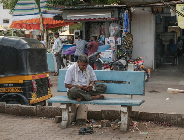 A busy street in Aurangabad with a man sitting on a bench, using his phone.