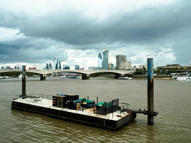 View of the River Thames and London skyline with a moody sky, featuring modern architecture and a bridge.