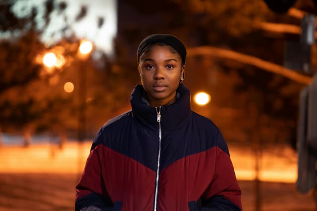 A woman stands confidently in a winter jacket under streetlights.