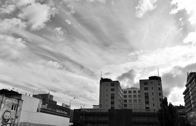 Black and white urban skyline of Dunedin, New Zealand with dramatic clouds.