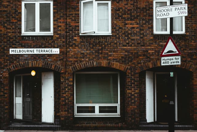 Facade of old brick residential building with plastic windows and jalousie near road with sign
