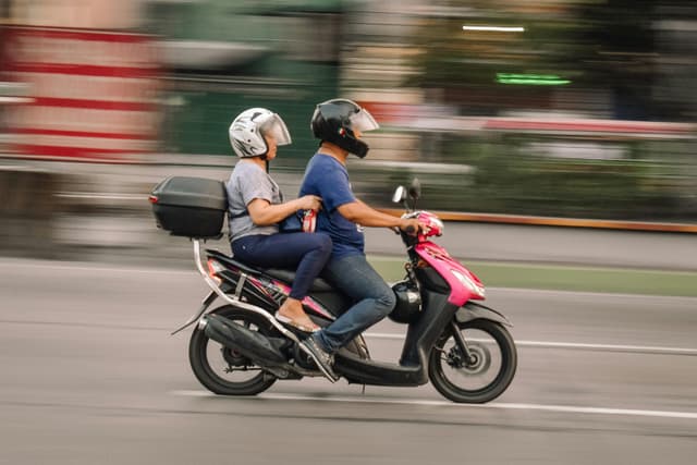 A couple riding a pink scooter in motion on bustling streets of Caloocan, Philippines.